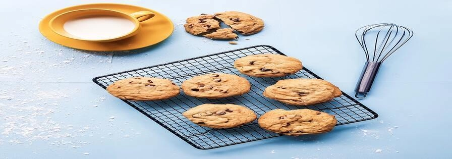 Some cookies on a plate, with bowl and a baking equipment on the side